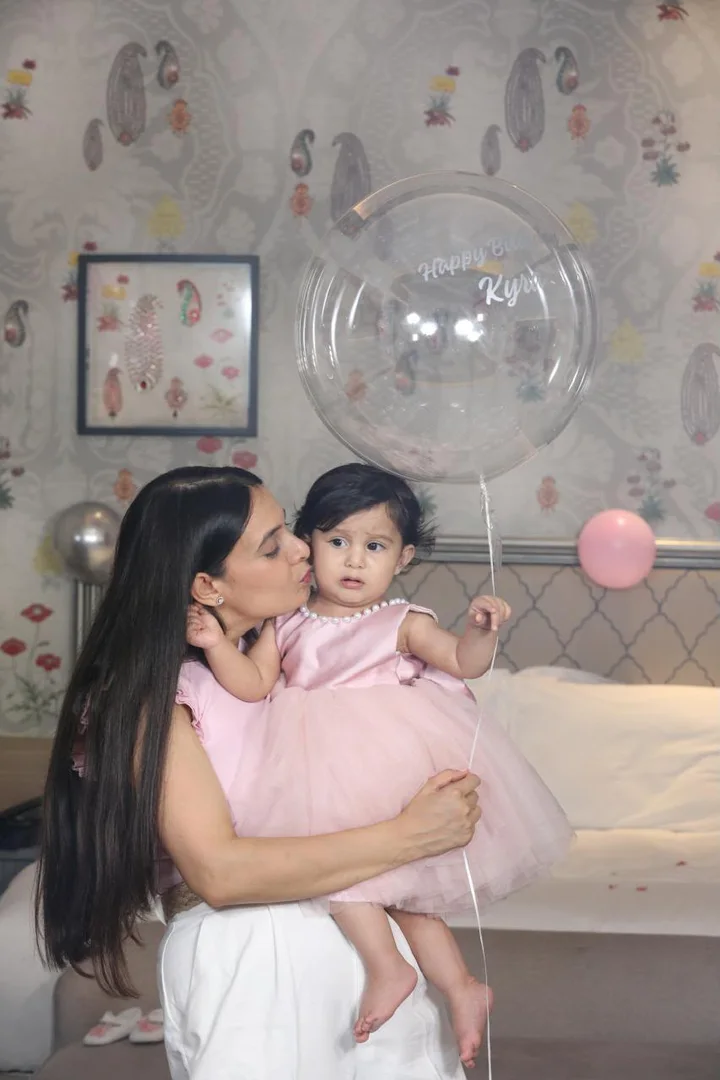 A mother kissing her daughter, who wears a pink dress, at a birthday celebration