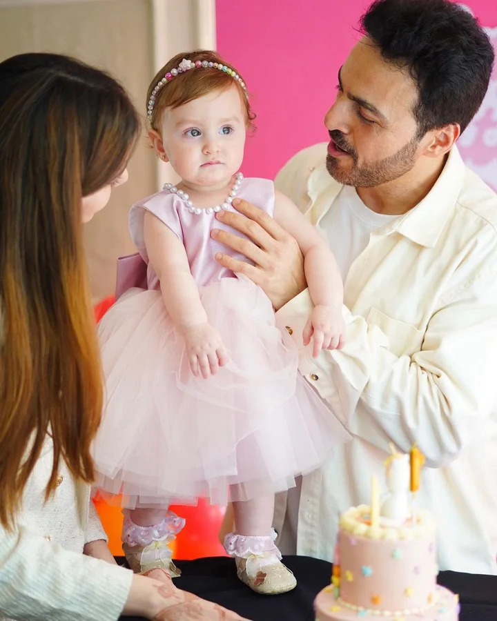 A little girl in her pink dress beside her birthday cake, held by her parents