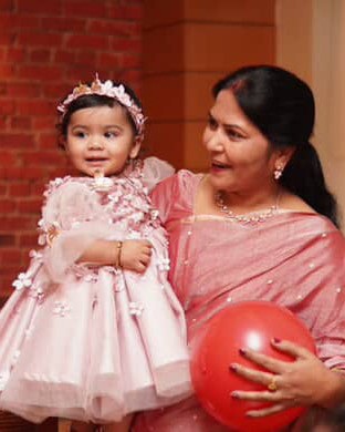 A woman in a pink sari holding a little girl in a blush flower dress and flower crown