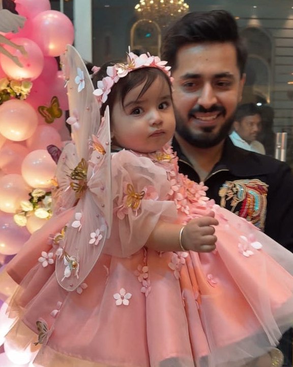 A father holding his daughter in a pink butterfly-wing Babiesfrock dress at a balloon party
