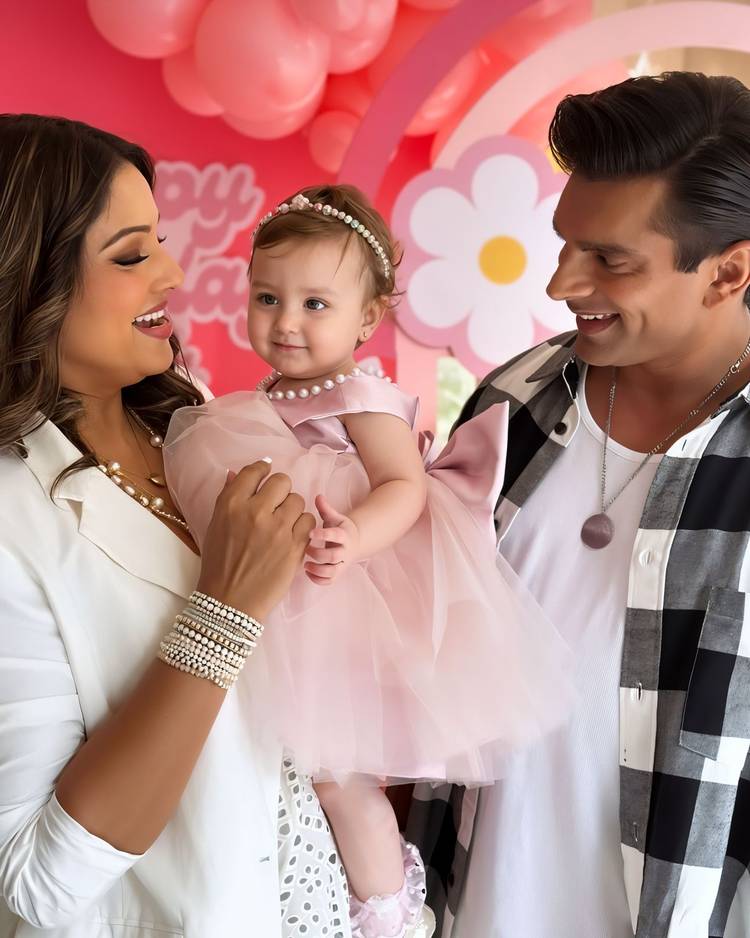 Parents smiling at their daughter in a blush pearl-trimmed Babiesfrock dress at her birthday