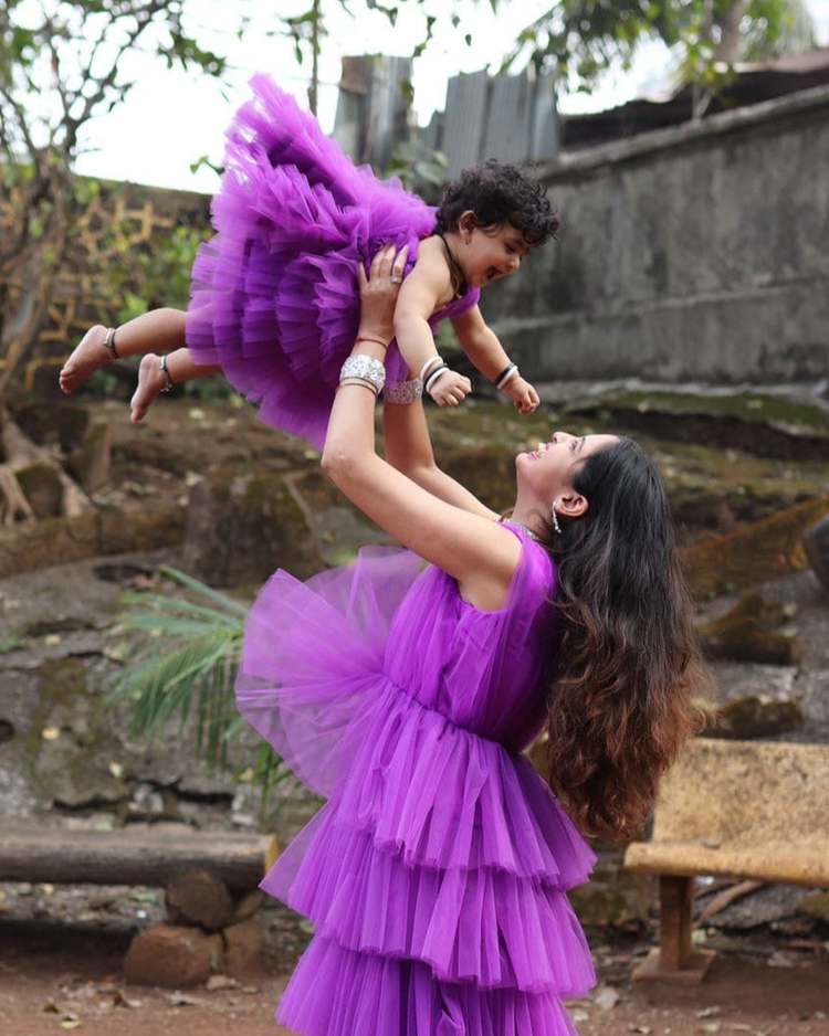 A mother lifting her daughter high outdoors, both in matching purple tiered tulle