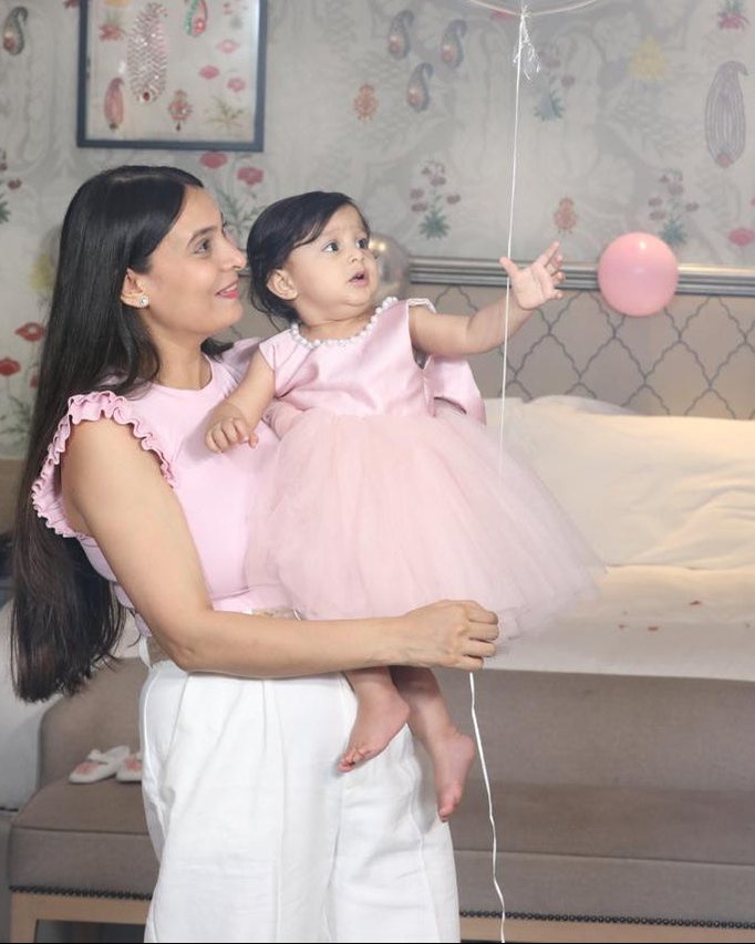 A mother holding her daughter in a blush tulle Babiesfrock dress as she reaches for a balloon